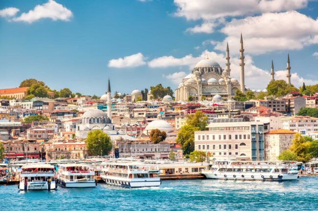 Touristic sightseeing ships in Golden Horn bay of Istanbul and view on Suleymaniye mosque with Sultanahmet district against blue sky and clouds. Istanbul, Turkey during sunny summer day.